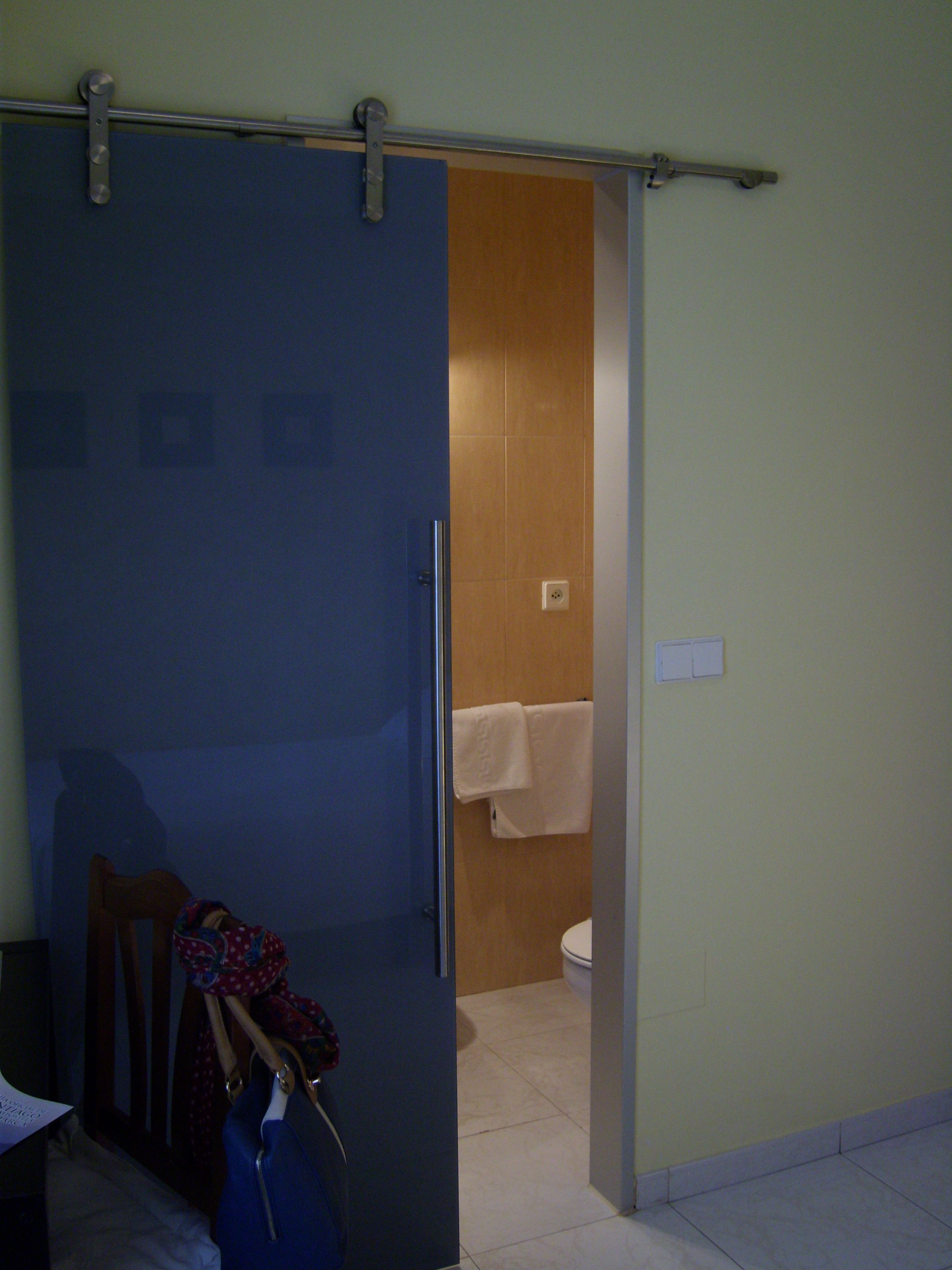 Une pièce avec une porte bleue, une porte en bois donnant accès à une salle de bain, et des toilettes blanches.