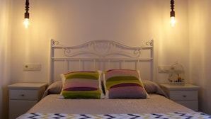 A bed with a white headboard, two bedside tables, and a nightstand with a birdcage. - Pensión Residencia Tambre (Santiago de Compostela)