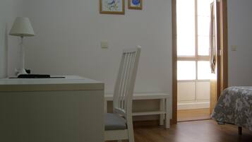 A room with a desk, chair, bed, and a door leading to another room.