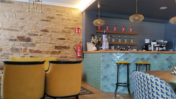 A cozy bar area with a stone wall, wooden counter, and yellow chairs. - Pensión Residencia Tambre (Santiago de Compostela)