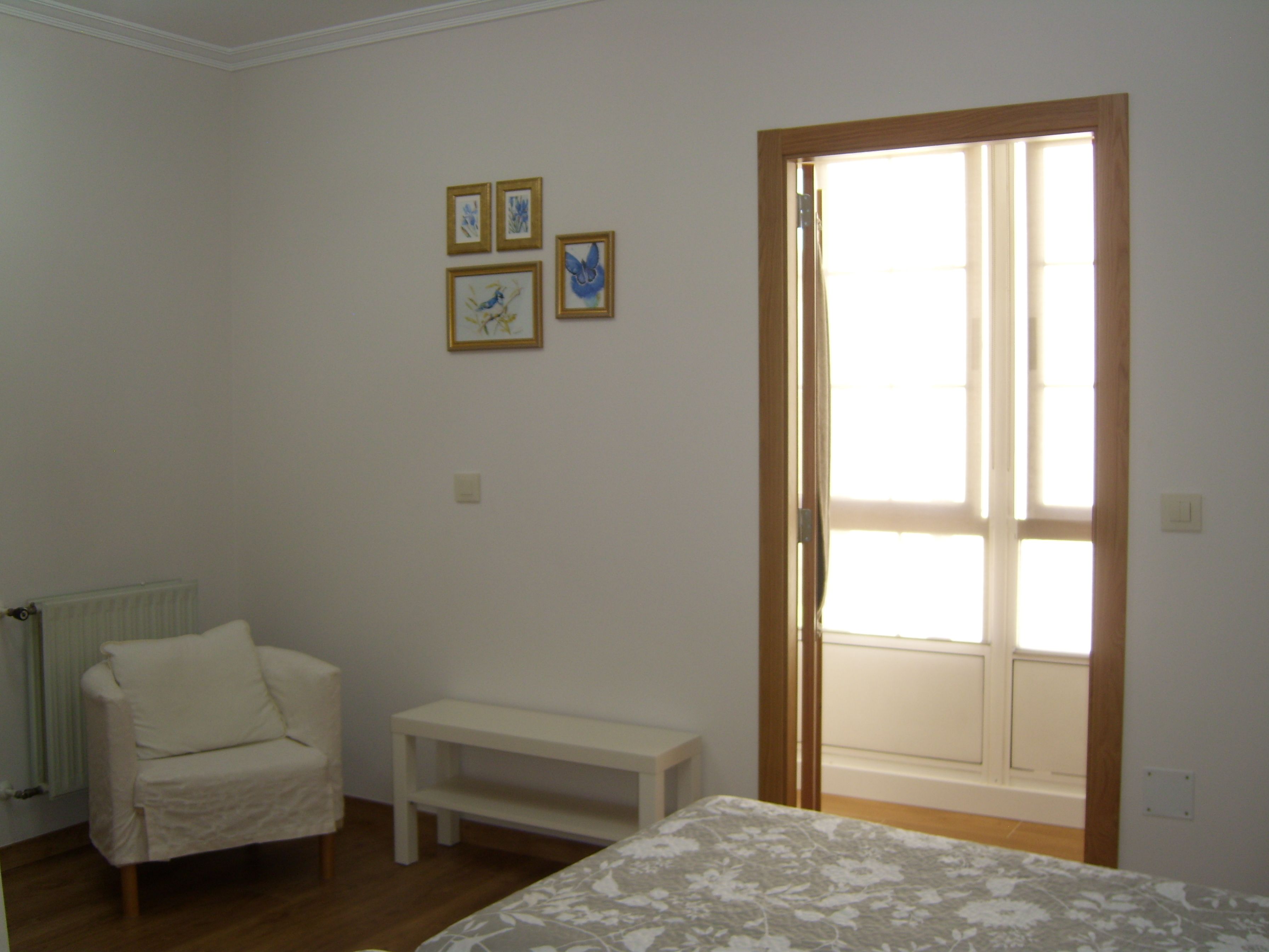 Un dormitorio con una cama, una silla, un banco y una puerta que da a un balcón.