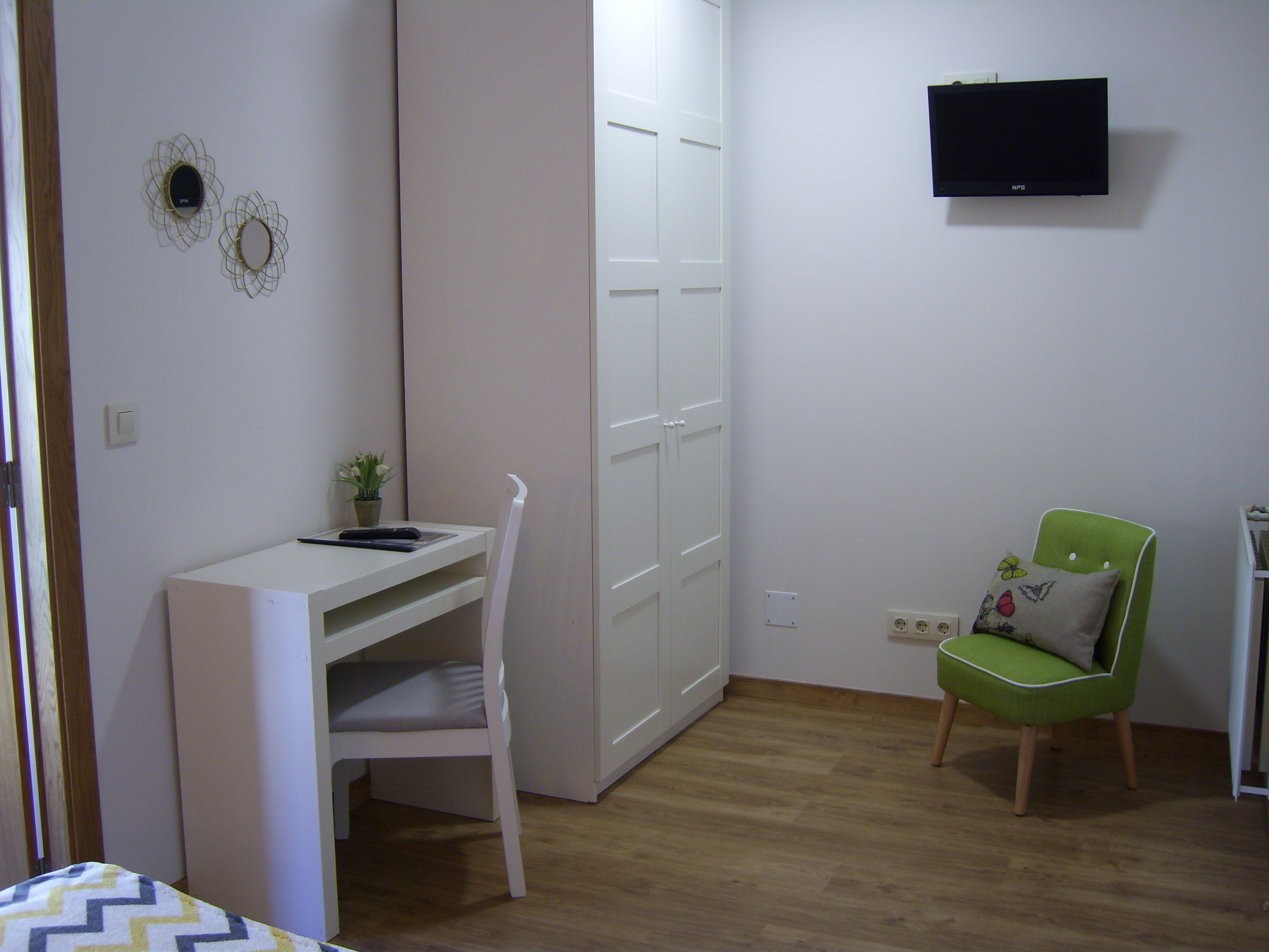 A small, neatly organized room with a white desk, a green chair, and a TV mounted on the wall.