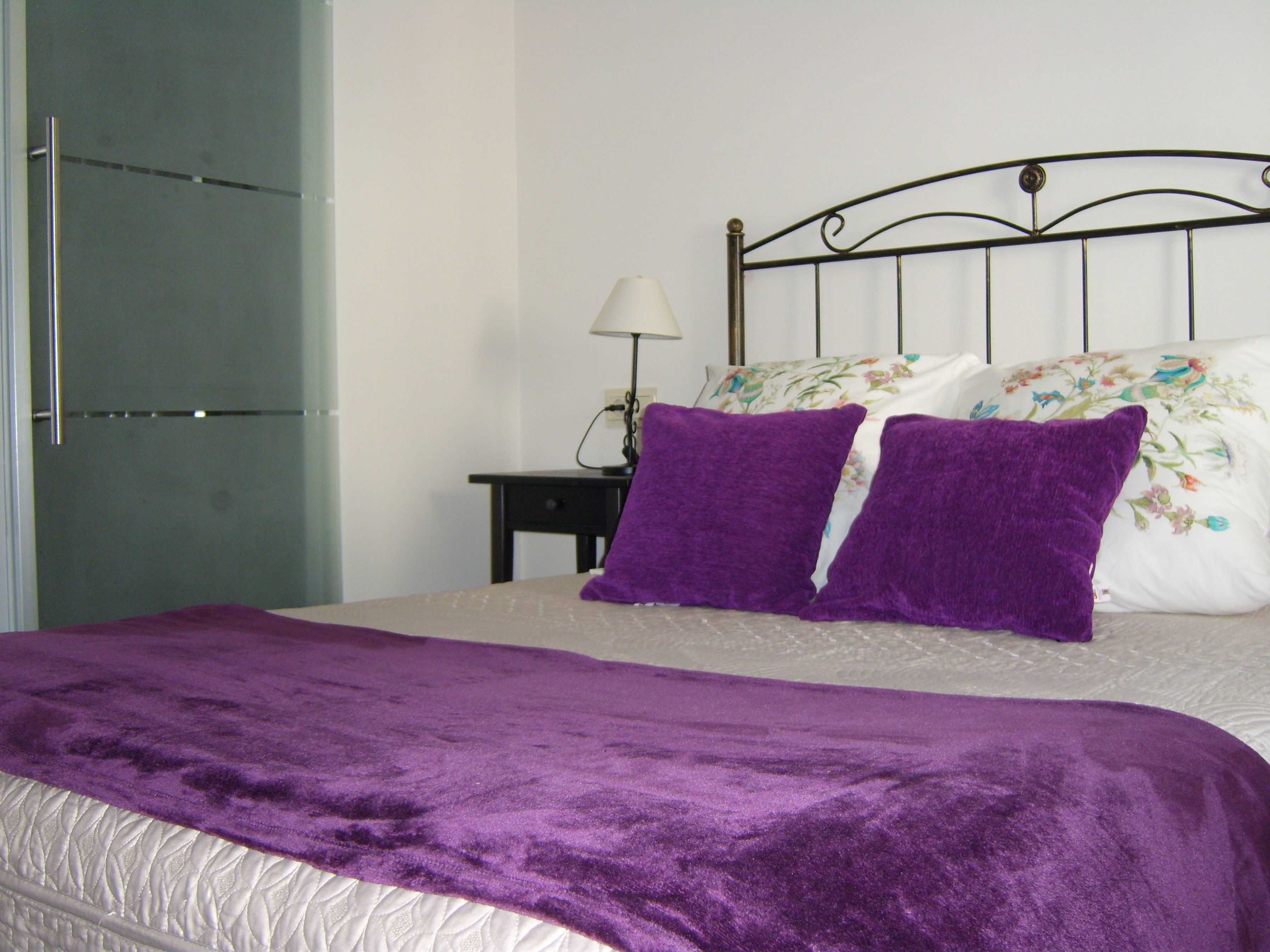 A bed with a purple blanket, a floral pillow, and a white pillow.