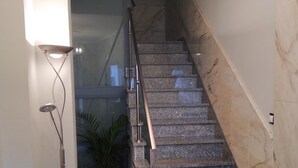 A staircase with a marble finish, a modern chair with a bird design, and a floor lamp. - Pensión Residencia Tambre (Santiago de Compostela)