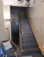 Una escalera con acabado de mármol, una silla moderna con diseño de pájaro y una lámpara de pie.