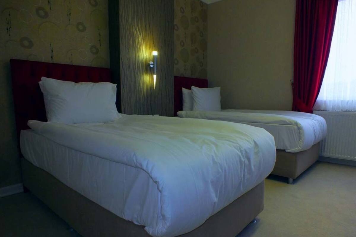 A hotel room with two beds, a red curtain, and a wall-mounted light fixture.