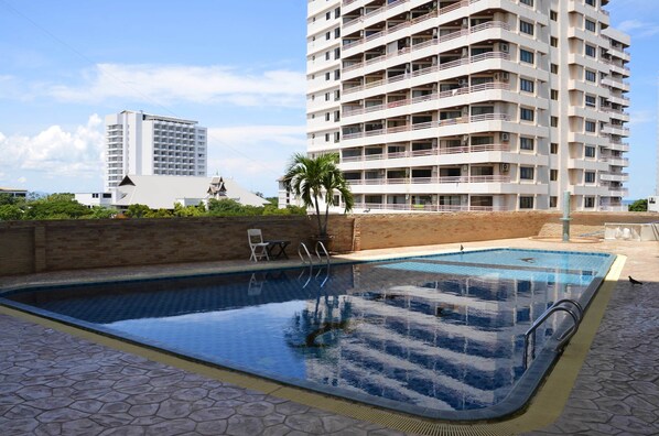 Una piscina con borde de baldosas, una palmera y un edificio alto al fondo.