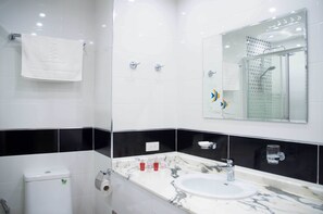Un baño moderno con pared de azulejos blancos y negros, un espejo grande, un lavabo con encimera de mármol y una zona de ducha.