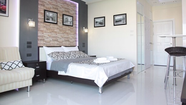 A modern bedroom with a brick accent wall, a large bed, a bedside table, a chair, and a small table with a chair.