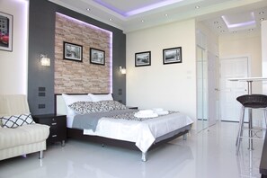 Un dormitorio moderno con una pared de ladrillo decorativa, una cama grande, una mesita de noche, una silla y una pequeña mesa con una silla.