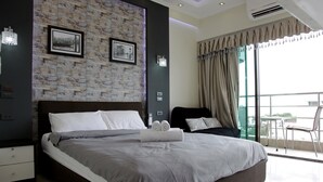 A modern bedroom with a large bed, a stone wall, and a balcony with a view.