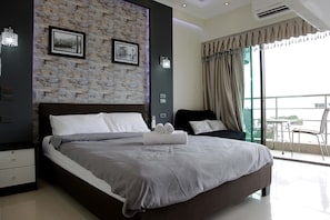 A modern bedroom with a large bed, a stone wall, and a balcony with a view. - ThepThip ArtDeco Apartments (Pattaya)