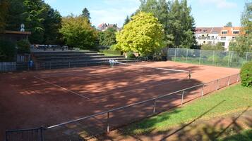 Una cancha de tenis con una red, rodeada por una valla y árboles.