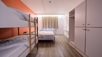 Een studentenkamer met stapelbedden, een raam met gordijnen, een radiator en een kledingkast.