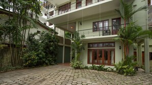 Un edificio de varios pisos con un patio central, pavimentado con piedras hexagonales, rodeado de abundante vegetación y diversas plantas.