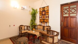 Un comedor con una mesa y sillas de madera, un adorno colgante en la pared, una planta en maceta y una puerta con un número.