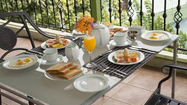Una mesa de desayuno en un balcón con vistas a zonas verdes, que incluye una barandilla de metal y un pilar verde.