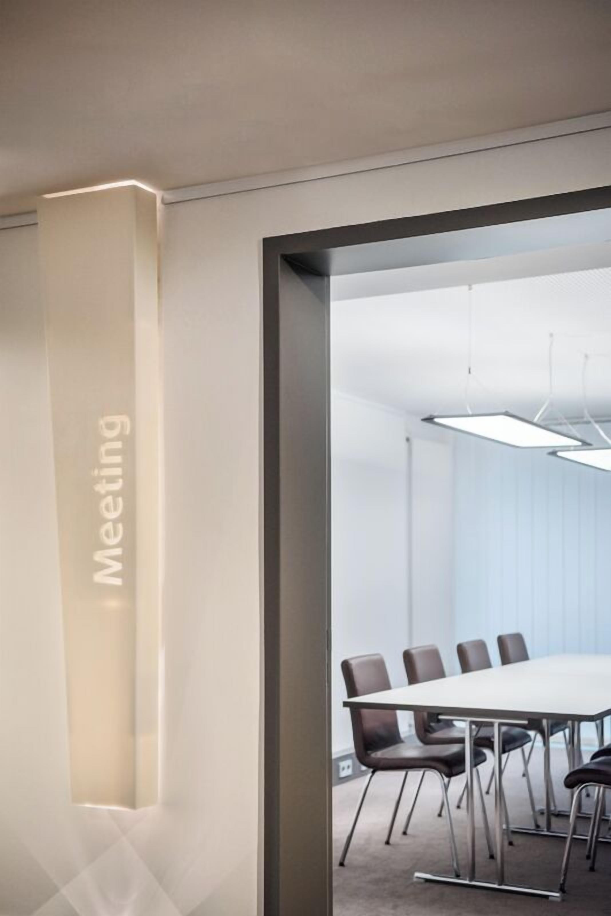 Una sala de reuniones moderna con una mesa larga y sillas, un divisor de vidrio y un cartel que indica el propósito de la sala.