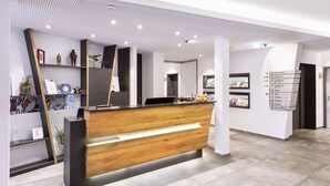 A modern hotel reception area with a wooden reception desk, a digital directory, and a clean, contemporary design. - HGS3 Konzept-Hotel (Schelklingen)