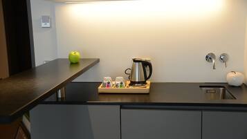 Una cocina moderna con encimera negra, una tetera, una cafetera y una manzana.