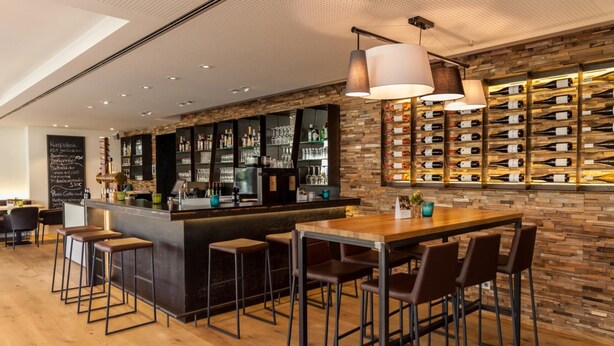 A modern bar area with a wooden bar counter, stools, and a wine rack. - HGS3 Konzept-Hotel (Schelklingen)