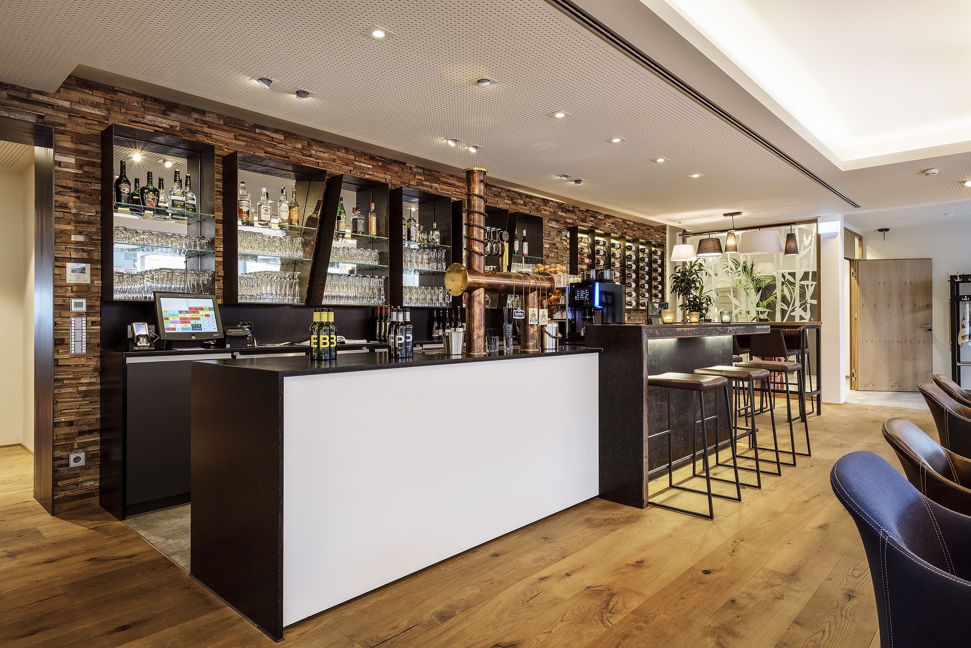 A modern bar area with a wooden wall, shelves of bottles, and a bar counter.