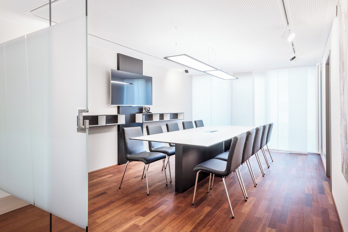 A conference room with a long table, chairs, a mounted TV, and a ceiling light fixture.