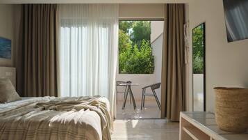 Un dormitorio moderno con una cama grande, una pequeña mesa con sillas y vistas a la vegetación a través de una puerta abierta.