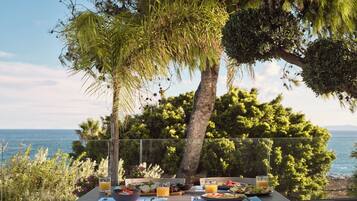 An outdoor dining table with breakfast items, overlooking a scenic view of the sea and trees.