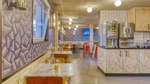 A restaurant with a patterned wall, a blue 'ek' sign, and a kitchen area with a coffee machine. - UNISOTEL Le Havre (Le Havre)