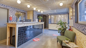 A reception area with a counter, a laptop, a potted plant, and a seating area with a magazine. - UNISOTEL Le Havre (Le Havre)