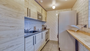 A modern kitchen with wooden cabinets, a stainless steel sink, a microwave, and a refrigerator. - UNISOTEL Le Havre (Le Havre)