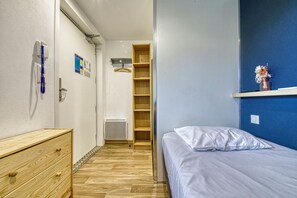 A bedroom with a bed, a wooden dresser, a shelf with a vase, and a blue wall. - UNISOTEL Le Havre (Le Havre)