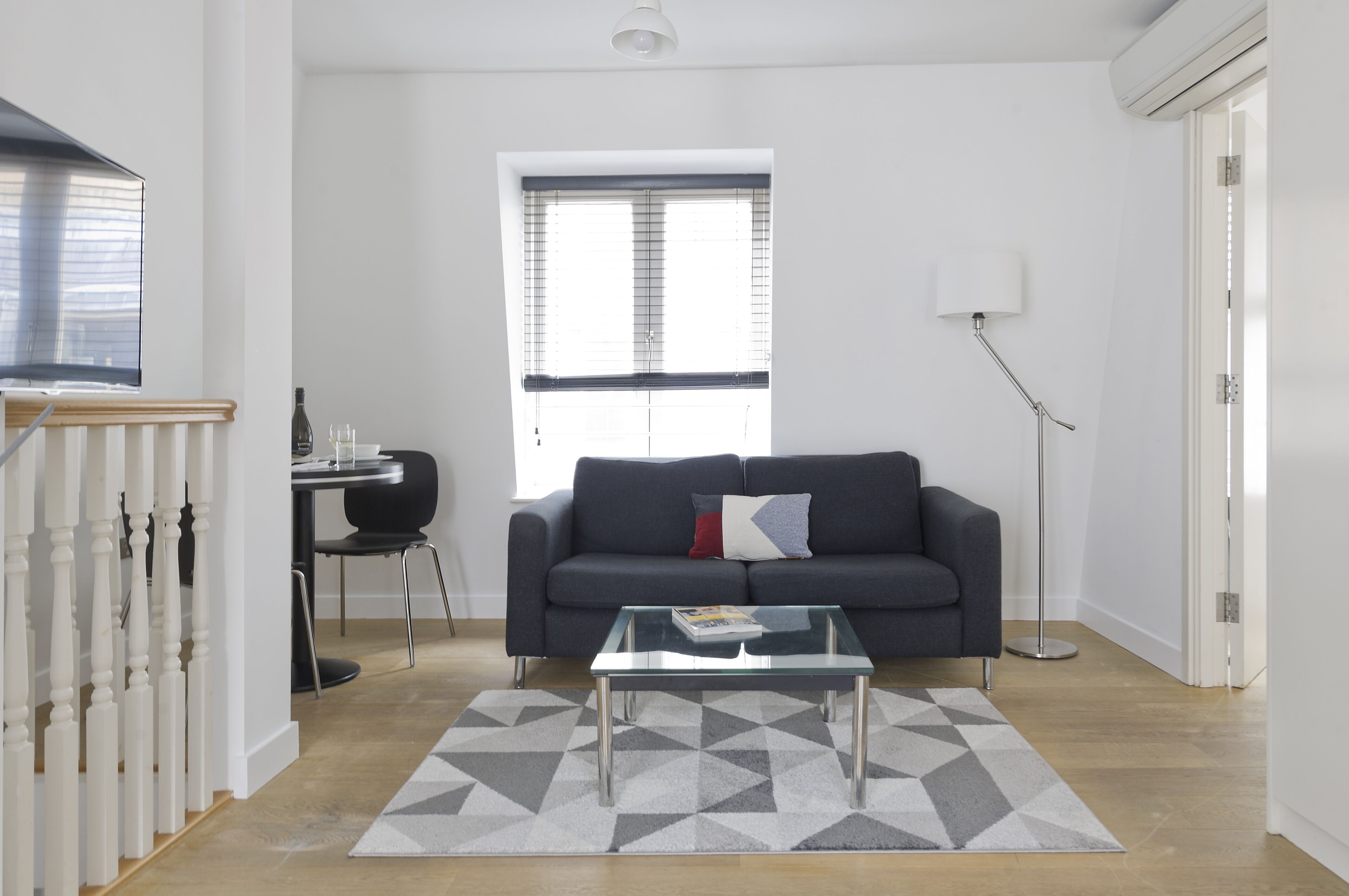 A modern living room with a dark grey sofa, a glass coffee table, and a geometric rug.
