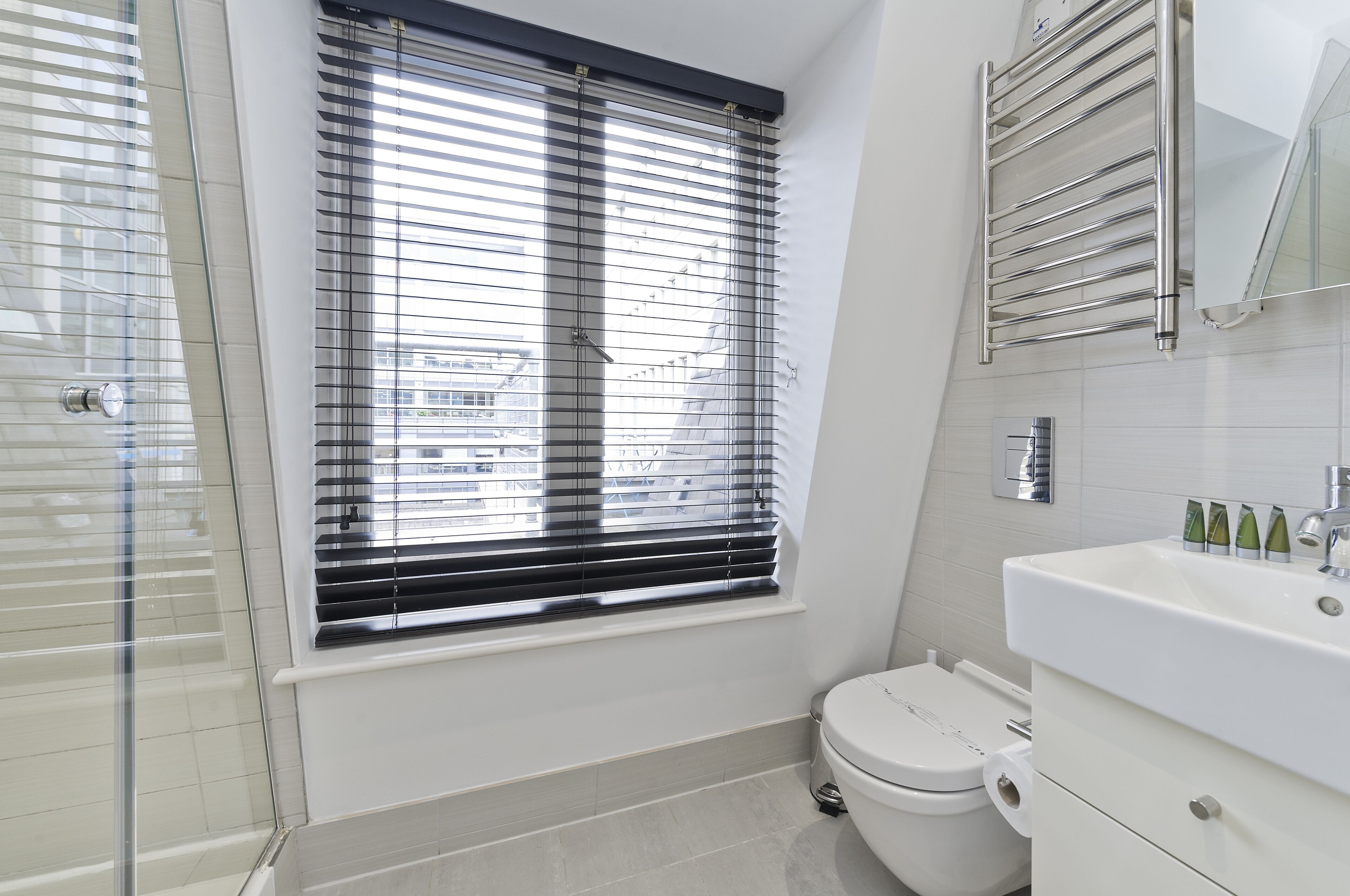Un baño moderno con inodoro, lavamanos y ventana con persianas.