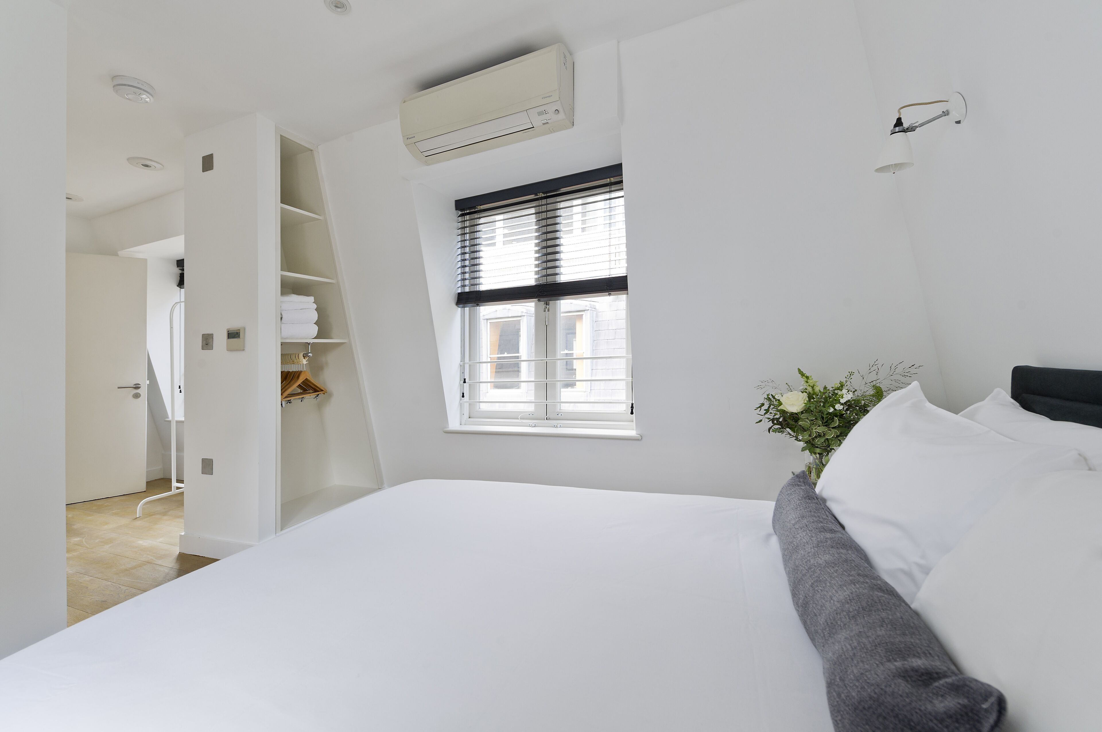 Una habitación de hotel moderna con una cama grande, una ventana con persianas, un armario empotrado y un equipo de aire acondicionado.