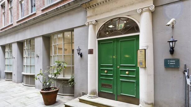 Un edificio con una puerta verde, un letrero que dice "Crane Court" y una planta en maceta en la entrada.