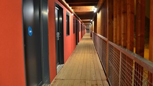 A corridor with doors on the left, wooden flooring, and a metal railing on the right. - Unisotel Le Mans (Le Mans)
