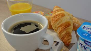A cup of coffee with a spoon, a croissant, a glass of orange juice, and a container of yogurt on a wooden table.