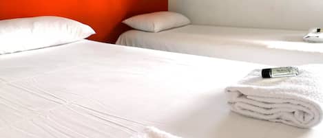 Habitación de hotel con dos camas, ropa de cama blanca y una toalla doblada sobre una de ellas.