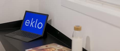A laptop on a desk with a window view, a bottle, and a framed picture.