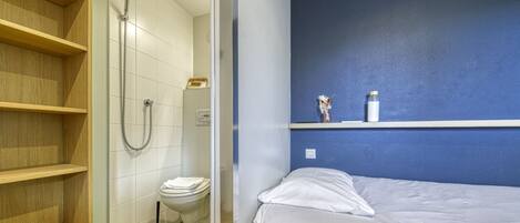 A bathroom with a shower, toilet, and a bed with a blue wall and shelves.