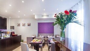 A hotel dining area with tables, chairs, a reception desk, and a large vase of flowers. - Hôtel Jenner (Paris)