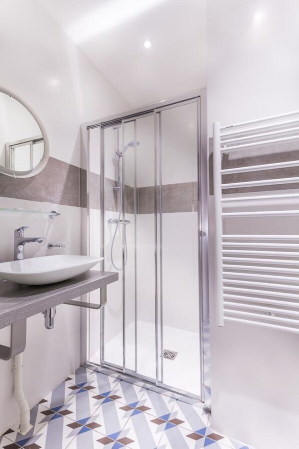 A modern bathroom with a glass shower enclosure, a white sink, and a towel rack.
