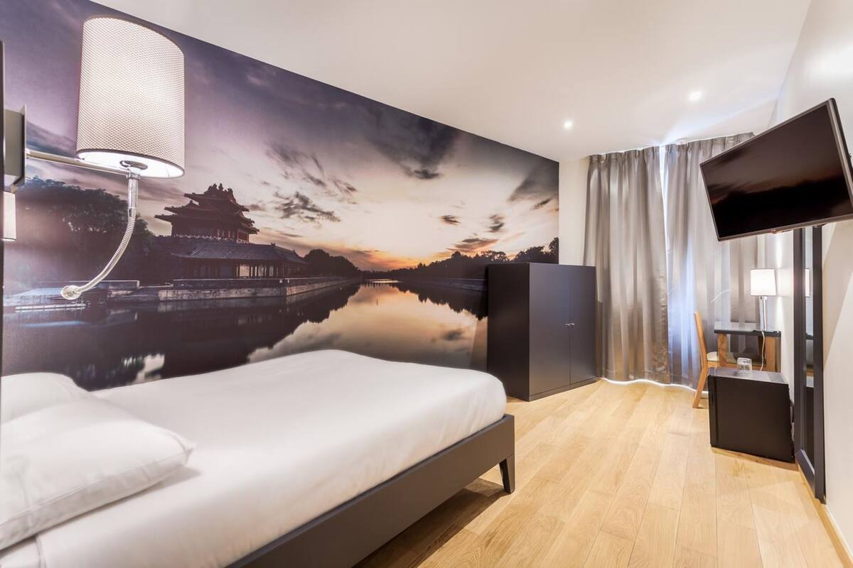 Una habitación de hotel moderna con una cama, un mural grande de una construcción tradicional, un televisor de pantalla plana y un escritorio con una lámpara.