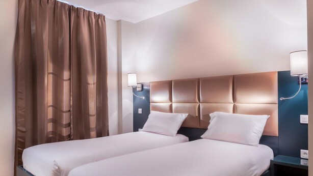 A hotel room with two single beds, a dark headboard, and a nightstand with a lamp. - Hôtel Jenner (Paris)