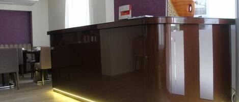 Una moderna recepción con cubierta de vidrio y acabado oscuro, una pequeña escultura de madera encima, y una pared morada de fondo.