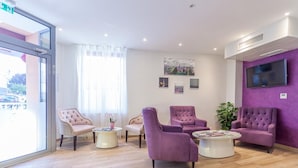 A modern reception area with plush seating, a TV, and artwork on the walls. - Hôtel Jenner (Paris)