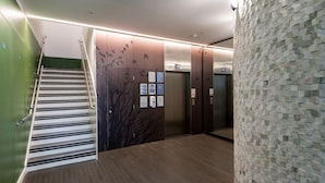A modern elevator area with a wooden floor, a green wall, and a wall with a bird mural. - Cove St Martin’s (London)