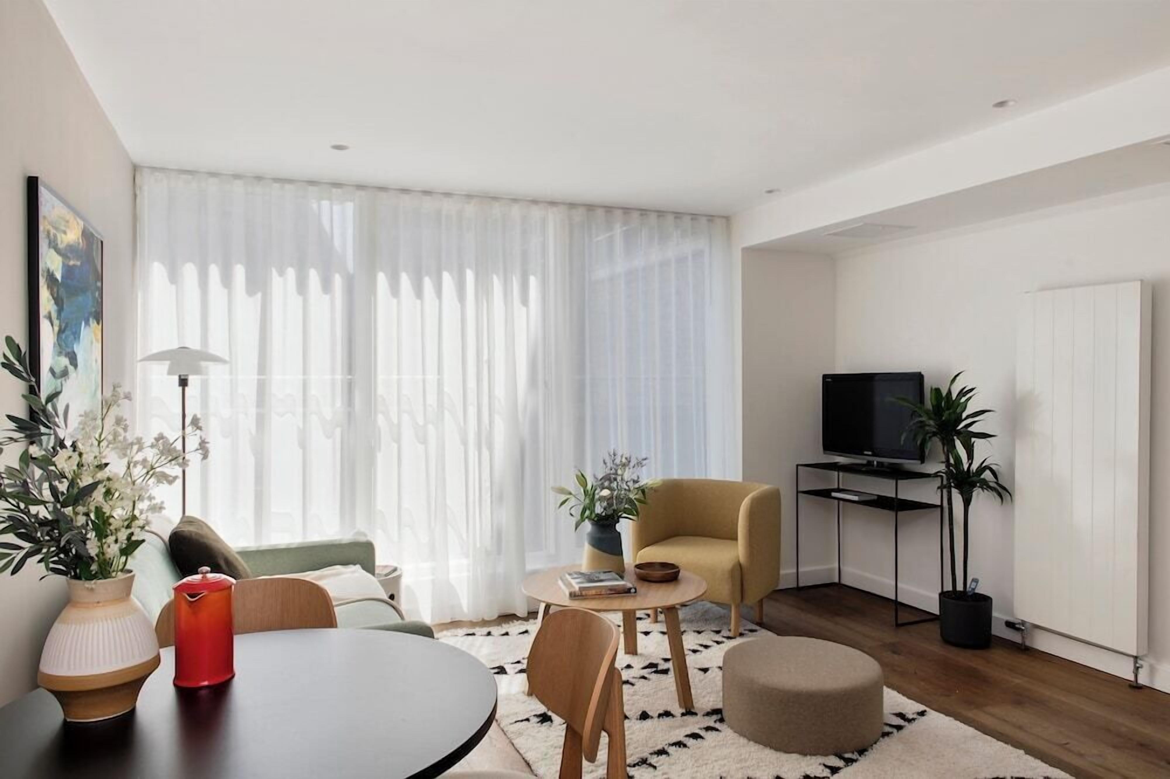 Een moderne woonkamer met een bank, een ronde tafel, een televisie op een dressoir en een potplant.